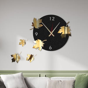 May include: A black and gold wall clock with a black background and gold leaf accents. The clock has a black face with white numbers and gold hands. The clock is surrounded by five gold leaves.