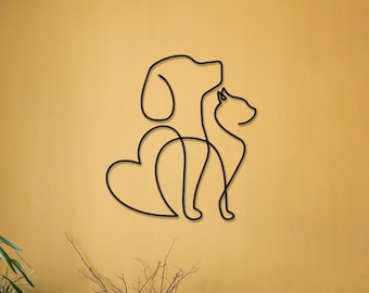 Könnte beinhalten: Schwarze Wandkunst aus Metall, die einen Hund und eine Katze in einem einzigen Linien-Design mit einer Herzform in der Mitte darstellt. Die Kunst ist an einer gelben Wand mit einem Holztisch und Pflanzen im Vordergrund montiert.