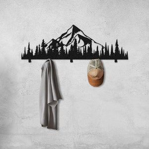 May include: Black metal wall-mounted coat rack shaped like a mountain range with trees. The rack has five hooks and is shown with a jacket and a hat hanging on it.