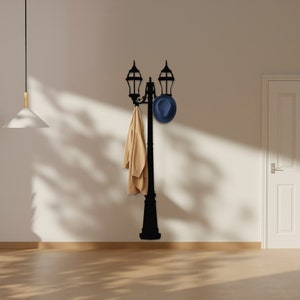 May include: Black metal wall-mounted coat rack shaped like a street lamp with a hat and coat hanging on it.