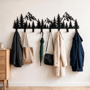 Può includere: Un appendiabiti da parete in metallo nero con la sagoma di una catena montuosa e una fitta foresta di pini. L'appendiabiti include otto ganci rivolti verso il basso, che sostengono un cappotto grigio scuro, una borsa beige, un ombrello verde, una borsa a tracolla nera, un cappotto beige e un cappotto blu scuro.