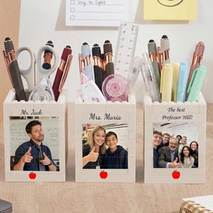 Puede incluir: Tres organizadores de escritorio rectangulares blancos construidos con bloques de plástico entrelazados. Cada uno presenta una foto personalizada, un nombre y un pequeño icono de manzana roja. El primero dice Mr. Jack, el segundo Mrs. Maria y el tercero The best Professor Hill.