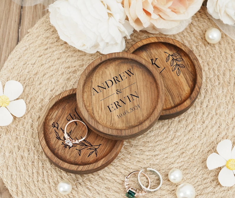 Peut inclure: Trois bo&icirc;tes &agrave; bagues en bois avec du texte grav&eacute;. La bo&icirc;te du haut indique "Andrew & Ervin 10.05.2024". La bo&icirc;te du milieu a un motif floral et la bo&icirc;te du bas a un "K" et un motif floral.