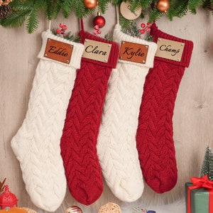 Op de afbeelding: Vier rode en witte gebreide kerstsokken met gepersonaliseerde houten naamschildjes. De namen op de naamschildjes zijn Eddie, Clara, Kylie en Champ.