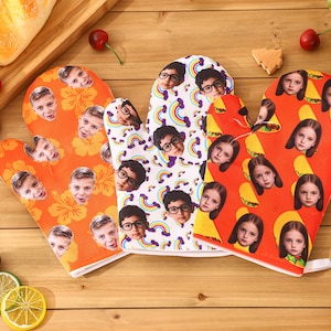 May include: Three oven mitts with custom face prints. One orange mitt features faces and hibiscus flowers. The second mitt is white with faces and rainbows. The third mitt is orange with faces and tacos.