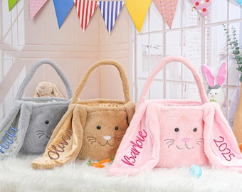 May include: Three plush bunny-shaped Easter baskets with embroidered names and the year 2025. The baskets are gray, brown, and pink.