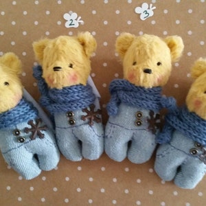 May include: Four yellow teddy bears wearing blue overalls and blue scarves. Each bear has a different number on a white tag.