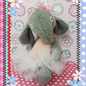 May include: A gray plush elephant wearing a pink tutu and a pink bow. The elephant is 6.5 inches tall and is sitting on a pink and white polka dot background. The image includes the text "6.5" Olleke elephant pattern" and "www.kattekopje.com".