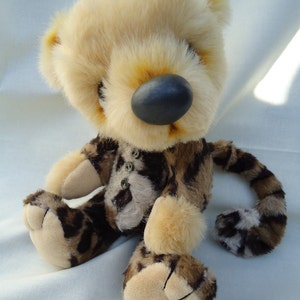 Puede incluir: Un oso de peluche beige y marrón con nariz negra y ojos de botón. El oso lleva un atuendo de estampado de leopardo.