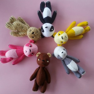 May include: A group of six plush toys, including a brown teddy bear, a pink bear, a yellow bear, a gray panda, a black and white panda, and a brown bear with a fluffy texture.