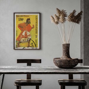 Pu&ograve; includere: Un poster vintage incorniciato con sfondo giallo che presenta una donna con un vestito rosso e bianco che balla. Il poster &egrave; intitolato "Kono - danse Bamanan" e "Republique du Mali" con il testo "150F" nell'angolo in alto a sinistra. Il poster &egrave; appeso a una parete bianca sopra un tavolo di legno con due sedie.