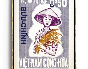 Op de afbeelding: Een vintage postzegel uit Vietnam met een vrouw in een kegelvormige hoed die een bos rijst vasthoudt. De postzegel is paars en wit met de tekst "Phu-Nu Viet-Nam" en "Buu-Chinh" in het Vietnamees.