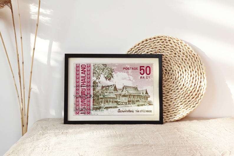 Op de afbeelding: Een ingelijste vintage Thaise postzegel met een rode rand en de tekst "ประเทศไทย THAILAND" en "POSTAGE 50 สด.ST." De postzegel toont een gedetailleerde illustratie van een traditioneel Thais huis.