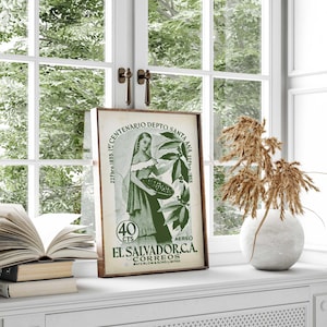 May include: A framed vintage El Salvador stamp, featuring a woman holding a basket, with text in Spanish. The stamp is green and brown, set against a window with a white frame and a view of green foliage.