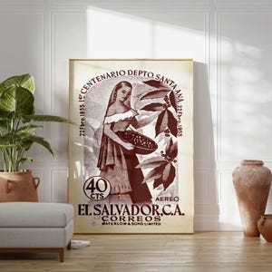 May include: A framed vintage poster featuring a woman holding a basket of coffee beans, with text in Spanish. The poster is in shades of brown and beige, with the text "EL SALVADOR.C.A. CORREOS". The poster is propped against a white wall.