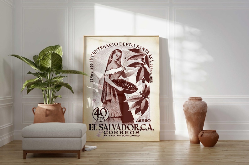 May include: A framed vintage poster featuring a woman holding a basket of coffee beans, with text in Spanish. The poster is in shades of brown and beige, with the text "EL SALVADOR.C.A. CORREOS". The poster is propped against a white wall.