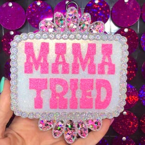 May include: A white and silver glitter sign with a pink glitter border and the words "MAMA TRIED" in pink glitter letters.