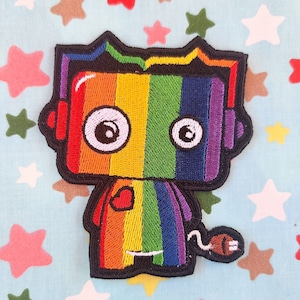 May include: Rainbow colored embroidered iron-on patch of a robot with a heart on its chest and a tail with a plug on the end.