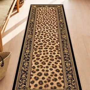 Könnte beinhalten: Ein rechteckiger Läuferteppich mit Leopardenmuster. Der Teppich hat einen schwarzen Rand mit goldenen, verzierten Details. Der Leopardenprint zeigt braune Flecken auf beigem Hintergrund. Der Teppich liegt auf einem hellen Holzboden.