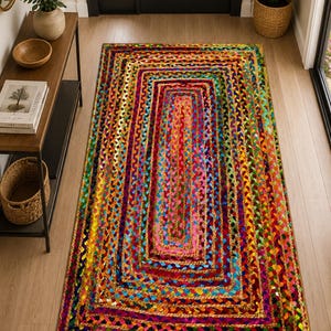 May include: A rectangular area rug featuring a vibrant, multi-colored braided pattern. The design consists of concentric rectangular borders in various hues including red, yellow, blue, green, and pink, created from woven fabric strips.