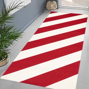 May include: A rectangular rug featuring broad, alternating red and white stripes. The rug is positioned on a light-coloured floor, with the stripes running along its length. The rug introduces a vibrant colour scheme and a contemporary design to the space.