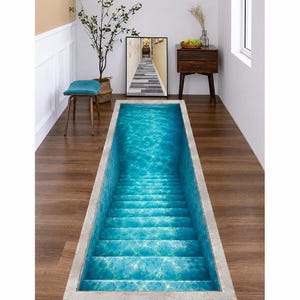 May include: A rectangular floor decal featuring a 3D optical illusion of a deep, turquoise swimming pool with submerged steps. The design displays realistic water ripples and light reflections, creating a visual effect of depth on a flat surface.