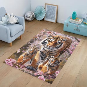 Pode incluir: Um tapete com um design floral rosa e branco com três tigres. A tigresa mãe caminha em direção ao espectador, enquanto os dois filhotes caminham atrás dela. O tapete é perfeito para adicionar um toque de natureza a qualquer cômodo.