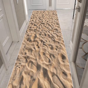 Könnte beinhalten: Ein rechteckiger Läuferteppich mit einem detaillierten Sandtextur-Design. Der Teppich ist hauptsächlich beige und braun und ahmt das Aussehen eines Sandstrandes nach. Er befindet sich in einem Flur mit weißen Türen und Wänden.