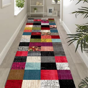 Könnte beinhalten: Ein rechteckiger Patchwork-Läuferteppich mit einer Vielzahl von Farben und Texturen. Der Teppich weist eine Mischung aus Quadraten in Rot-, Schwarz-, Blau-, Grün-, Gelb- und Grautönen auf. Der Teppich liegt auf einem hellen Holzboden.