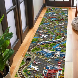 May include: A rectangular airport-themed rug featuring a detailed illustration of an airport with airplanes, trains, cars, and buildings. The rug has a green and gray color scheme with a winding road and railway track design.