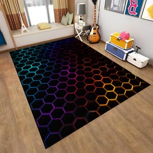 May include: A rectangular area rug with a black background and a vibrant, colorful honeycomb pattern. The pattern transitions from blue to purple, then to orange and yellow. The rug is placed on a wooden floor.