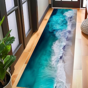 Peut inclure: Un tapis de sol rectangulaire représentant une scène océanique. Le design présente des eaux turquoise et bleu sarcelle avec des vagues blanches et mousseuses s'écrasant sur une plage de sable. Le tapis est placé dans une porte.