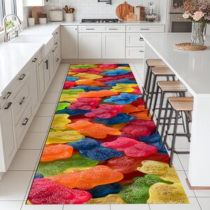Può includere: Un colorato tappeto runner da cucina con un motivo di caramelle gommose in vari colori, tra cui rosso, arancione, giallo, verde e blu. Il tappeto è rettangolare e posizionato in una cucina.
