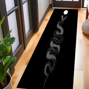 Könnte beinhalten: Schwarz-weißer Teppich mit einem grafischen Design einer Schlange, die zu einem weißen Kreis hinaufreicht. Die Schlange ist mit einem Sternenmuster verziert.