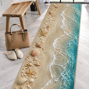 Puede incluir: Una alfombra rectangular con diseño de playa, que muestra una orilla arenosa con conchas marinas y estrellas de mar. La alfombra presenta un patrón de olas oceánicas turquesas, creando un ambiente costero. Para uso en interiores.