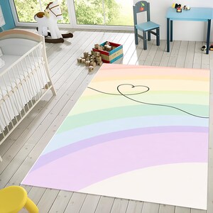 May include: A rectangular rug with a pastel rainbow gradient design. The rug features a black line drawing of a heart. The rug is in a child's room with a cot, rocking horse, and small table.