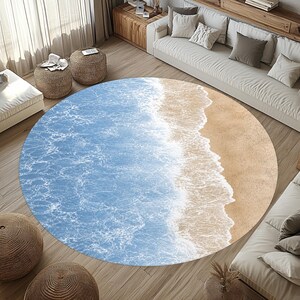 Peut inclure: Un tapis rond avec un motif de scène de plage. Le tapis présente un océan bleu clair avec des vagues blanches et mousseuses rencontrant une plage de sable beige. Le tapis est posé sur un sol en bois, entouré de meubles.