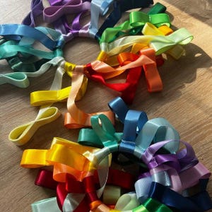 Peut inclure: Plusieurs rubans de satin colorés disposés en motifs circulaires. Les rubans présentent un spectre complet de couleurs, notamment le rouge, l'orange, le jaune, le vert, le bleu et le violet. Les rubans sont disposés sur une surface en bois brun clair.