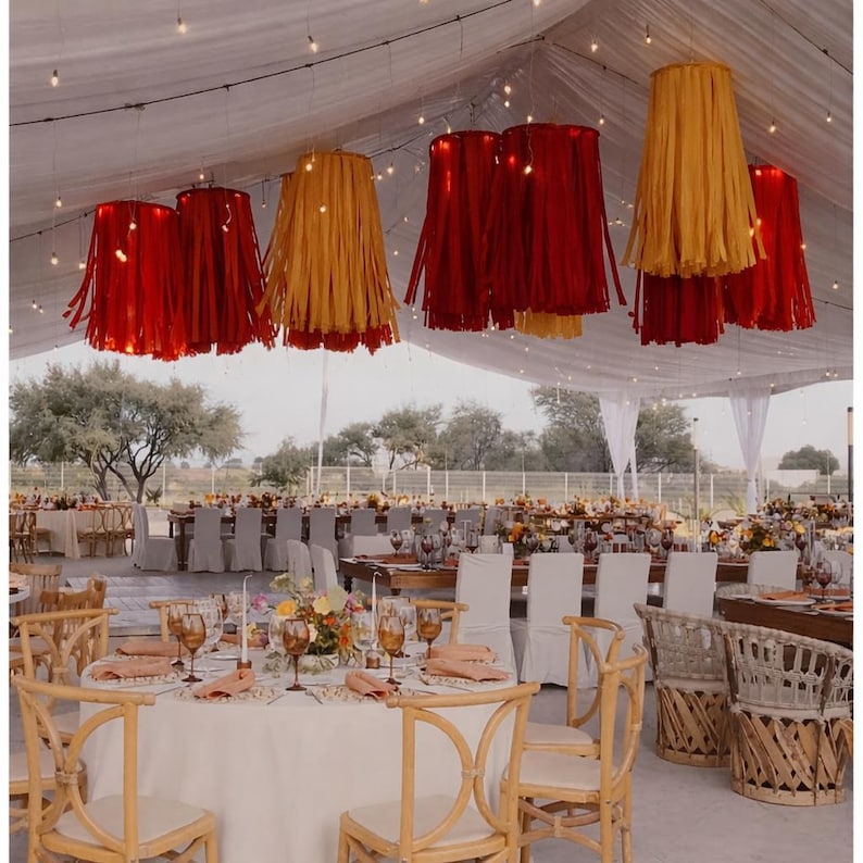 Peut inclure: D&eacute;coration de r&eacute;ception de mariage avec des tables et des chaises sous une tente blanche. Des lampes &agrave; franges rouges et jaunes sont suspendues au plafond. Les tables sont orn&eacute;es de centres de table floraux, de verres et de serviettes.