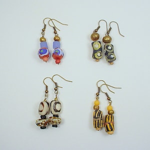 May include: Four pairs of dangle earrings with colourful glass beads. The earrings are made with brass wire and feature different patterns and colours.