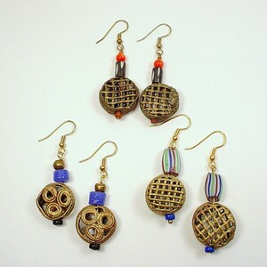 May include: A set of four pairs of earrings with gold-toned metal and colorful glass beads. The earrings feature a variety of designs, including a circular design with a woven pattern, a circular design with a spiral pattern, and a circular design with a beaded pattern.