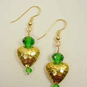 Puede incluir: Pendientes de corazón de oro con detalles de cristal verde. Los corazones son martillados y tienen un acabado texturizado.
