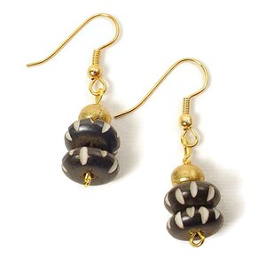 May include: A pair of gold earrings with black and white patterned beads. The earrings have a simple gold hook design.