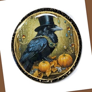 May include: A circular brooch featuring a black raven wearing a black top hat and a green jeweled collar. The raven is positioned above two orange pumpkins and autumn leaves, set against a background of hanging pearls and gold accents.