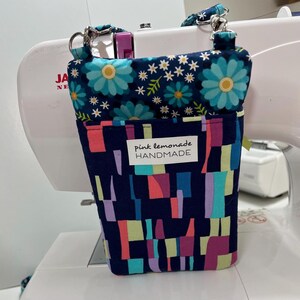 May include: A handmade fabric organizer with a floral top and geometric patterned body. The top features blue flowers and white stars on a navy background. The body has a navy base with colorful rectangles. The label reads "pink lemonade HANDMADE."