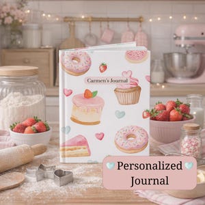 May include: A personalised journal with a white cover decorated with illustrations of donuts, cupcakes, cake slices, and strawberries. The journal has the text "Carmen's Journal" and "Personalized Journal". The background includes baking supplies and fresh strawberries.