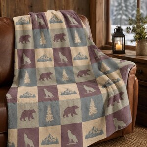 May include: A plush throw blanket featuring a repeating checkerboard pattern of cream, slate blue, and muted purple squares. Each square displays a nature-themed graphic of a bear, a howling wolf, a mountain range, or a pine tree in a contrasting colour.