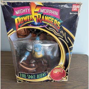May include: A vintage Mighty Morphin Power Rangers action figure in its original packaging. The box features the Power Rangers logo, the text "Evil Space Aliens," and the character name "Squatt." The figure is blue, silver, and yellow.