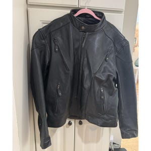 May include: Black leather jacket with a stand-up collar, multiple zipped pockets, and a front zip closure. The jacket is hanging on a pink hanger. The jacket appears to be made of a smooth, durable leather material.