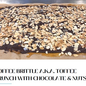 K&ouml;nnte beinhalten: Nahaufnahme eines Toffee-Br&ouml;sels mit Schokolade und Mandeln. Der Br&ouml;sel befindet sich auf braunem Backpapier und hat eine hellbraune Karamellbasis, eine Schicht dunkler Schokolade und ist mit Mandelbl&auml;ttchen belegt.